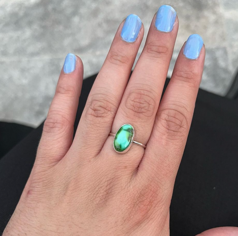 photo shows the hand of a white woman with a baby blue painted finger nails. She has a silver ring with an oval stone on her middle finger of her left hand. 